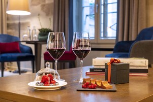 Una mesa de comedor con dos copas de vino, una tabla de quesos y un postre bajo una campana de cristal.