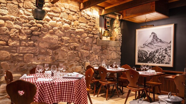A restaurant with stone walls, checkered tablecloths, and wooden chairs.