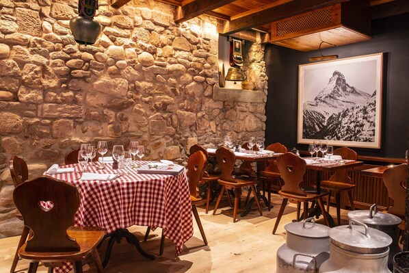A restaurant with stone walls, checkered tablecloths, and wooden chairs. - Hôtel Les Armures (Geneva)