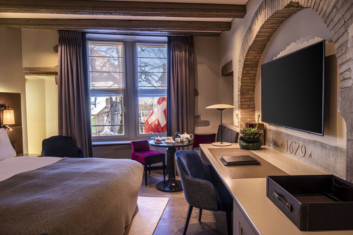 A hotel room with a bed, a desk, a chair, a TV, and a window with curtains.