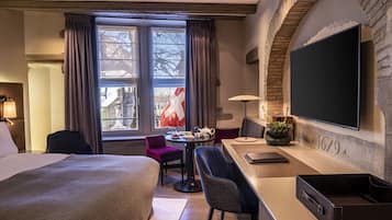 A hotel room with a bed, a desk, a chair, a TV, and a window with curtains.
