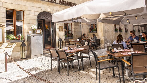 Un área de café al aire libre con mesas y sillas, un edificio de piedra con un letrero que dice 