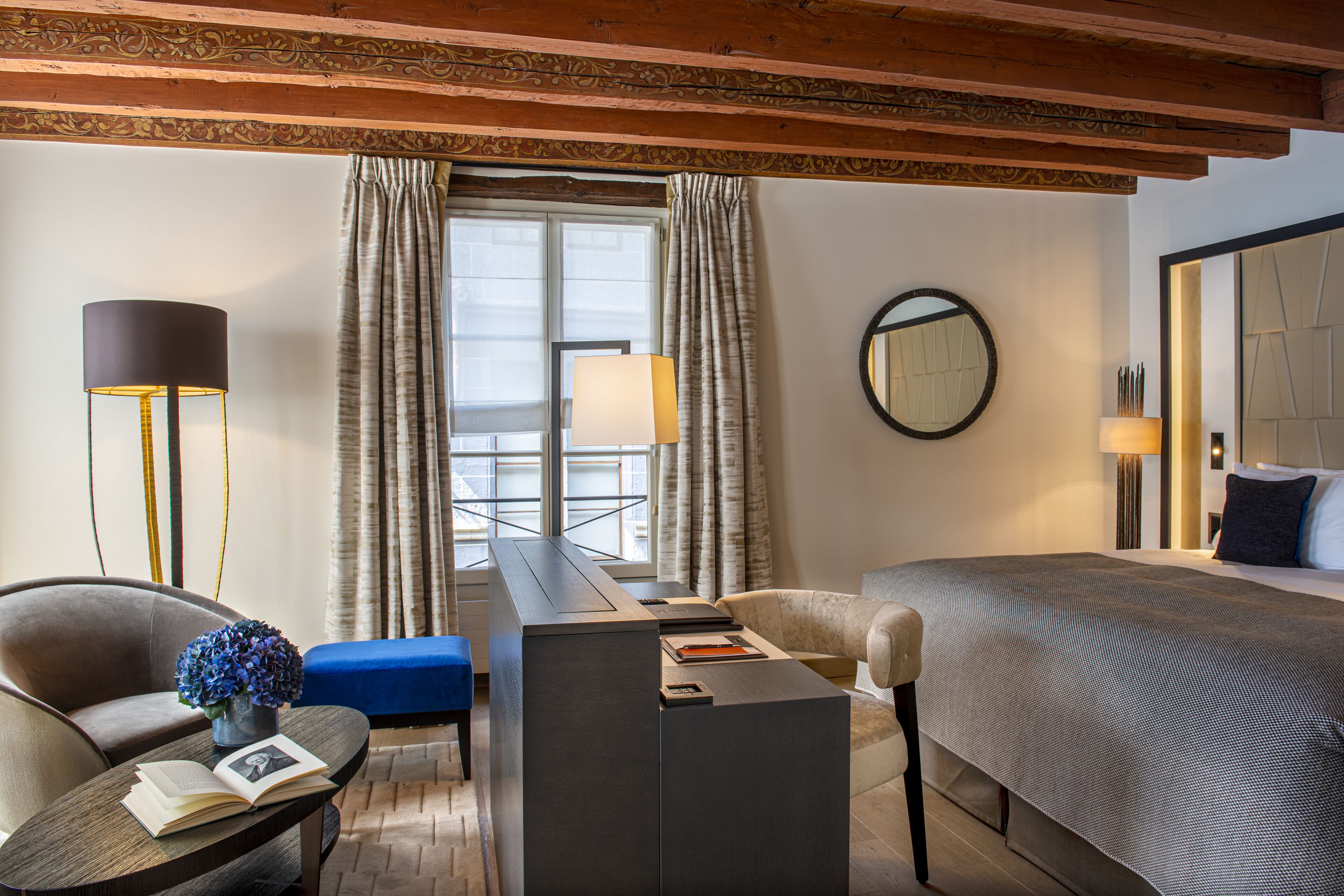 A hotel room with a bed, a desk, a chair, a sofa, and a lamp.