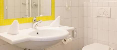 Un baño con lavamanos, espejo y inodoro blancos, paredes de azulejos amarillos y techo blanco.