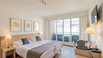 A hotel room with a large bed, bedside tables with lamps, a desk with a printer, and a TV on the wall.