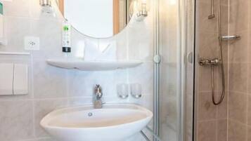 A modern bathroom with a glass-enclosed shower, a white sink, and a large mirror above it.