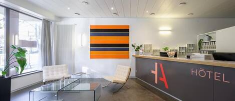 Un área de recepción de hotel moderna, con un mostrador de vidrio, dos sillones, una gran obra de arte abstracta y una recepción con el letrero 'HOTEL'.