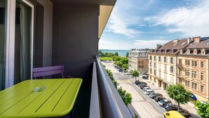 A balcony with a green table and a purple chair, overlooking a street with parked cars and buildings. - Hotel des Arts (Neuchatel)