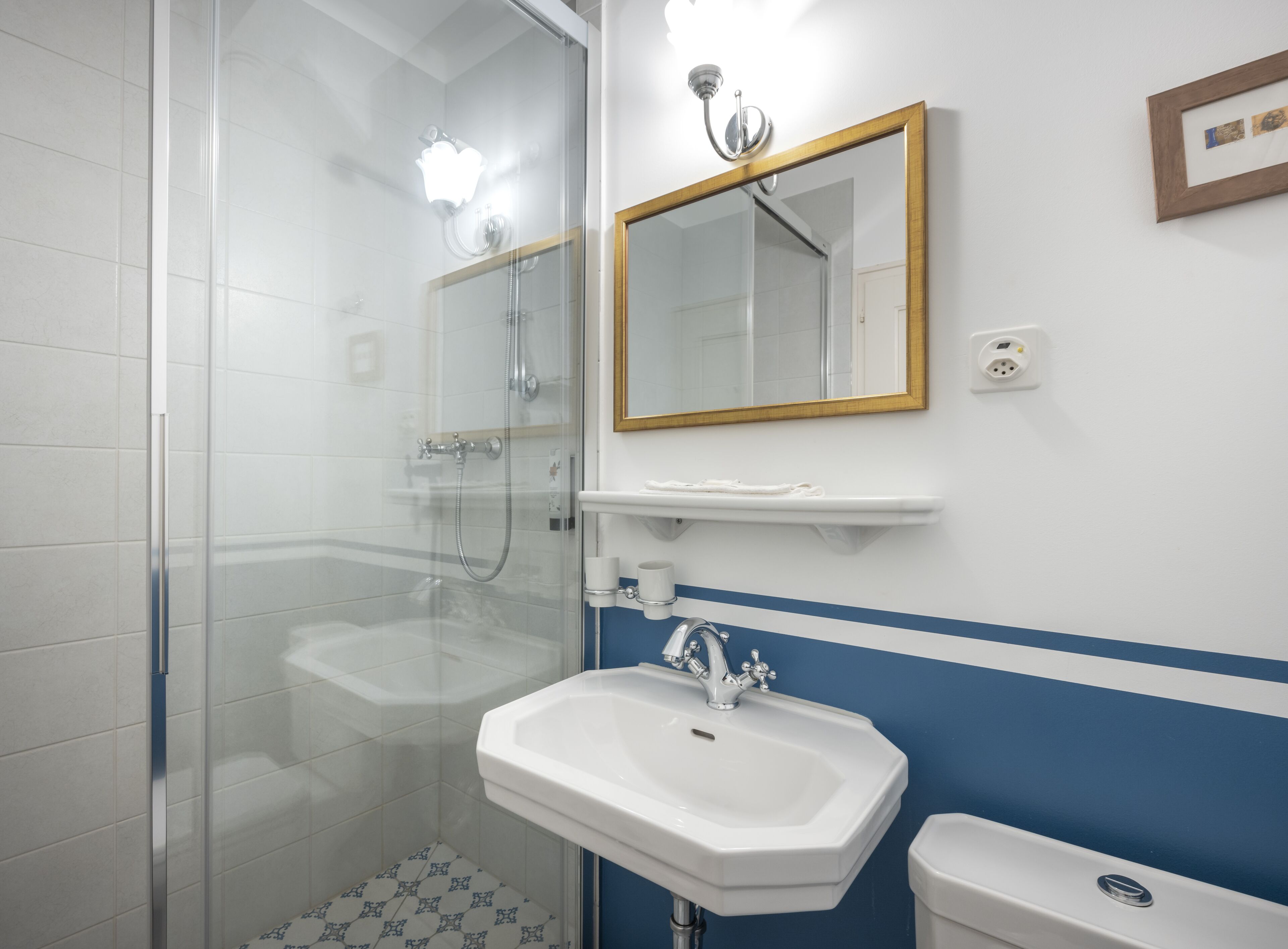 Een badkamer met een douchecabine van glas, een witte wastafel en een spiegel met gouden lijst.
