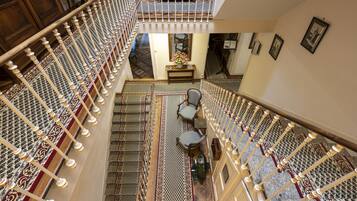 A grand staircase with ornate railings and patterned carpets, leading to a seating area with chairs and a table.