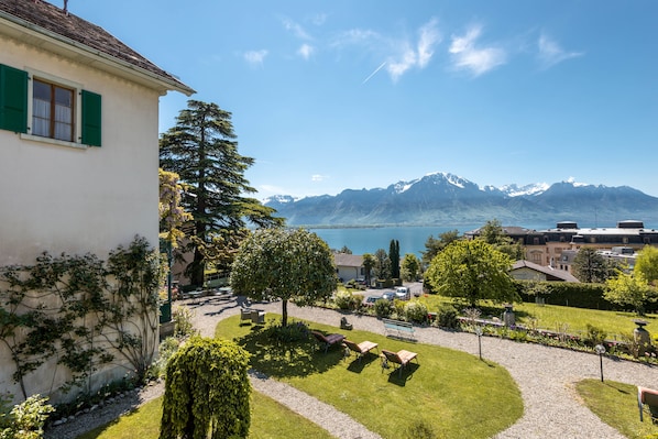A residential area with a house, a well-maintained garden, and a view of mountains and a lake. - Hôtel Masson (Veytaux)