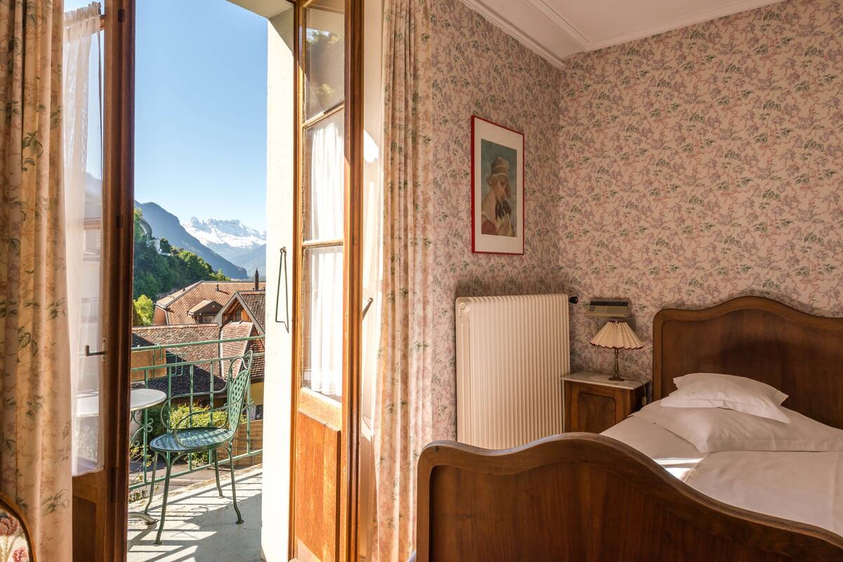 A bedroom with a wooden bed, a radiator, a small bedside table with a lamp, and a framed picture on the wall.