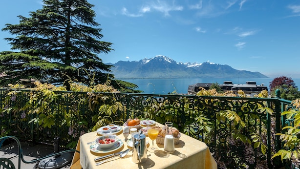 A table set with breakfast items overlooking a mountain and lake. - Hôtel Masson (Veytaux)