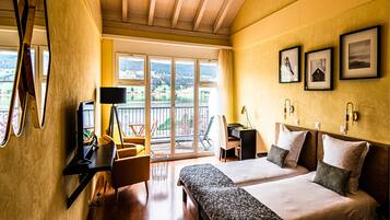 A hotel room with two beds, a desk, a chair, a TV, and a balcony with a view of the outdoors.