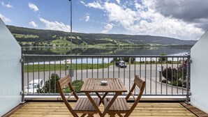 A balcony with a wooden table and chairs, overlooking a lake and a road with vehicles. - Hôtel Bellevue Le Rocheray (Le Chenit)