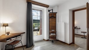 A modern room with a wooden desk, a chair, a hanging rack, and a view of the outdoors. - Hôtel Bellevue Le Rocheray (Le Chenit)