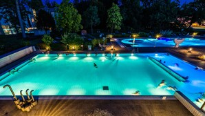 Una amplia piscina exterior con varias pistas, rodeada de árboles y tumbonas.