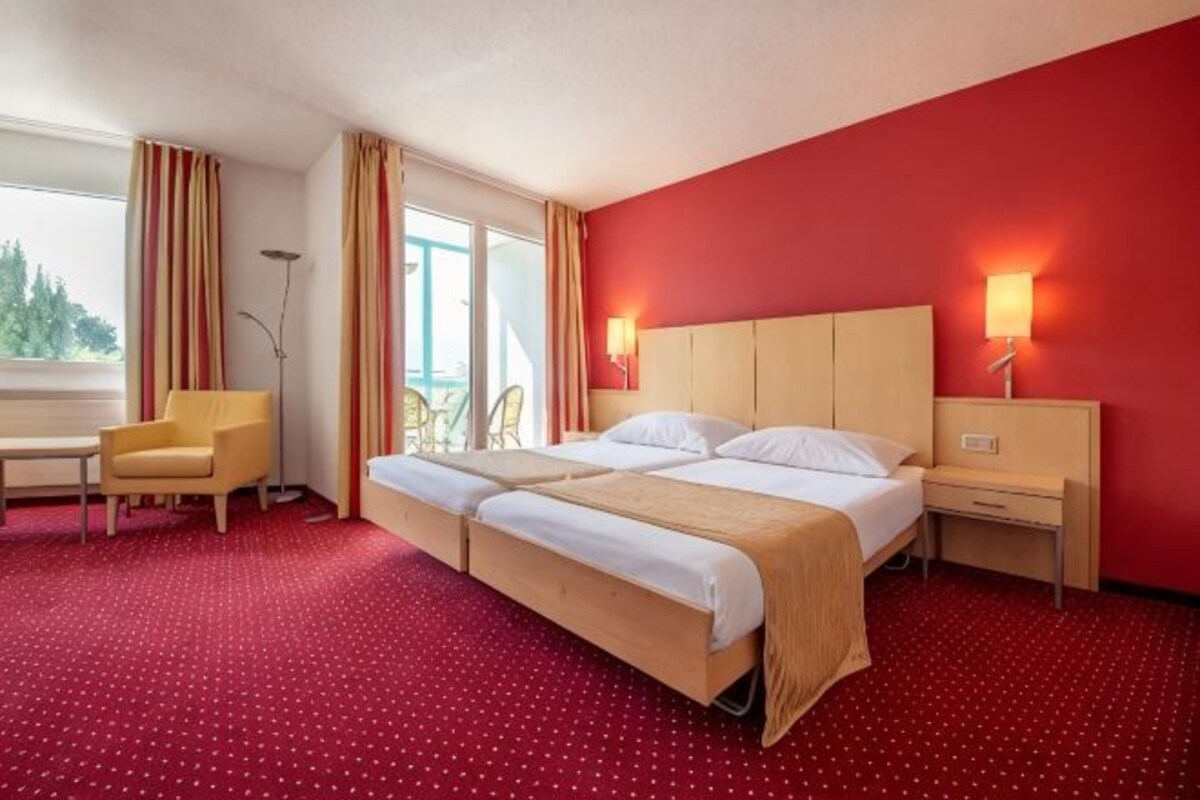 A hotel room with two beds, a desk, a chair, and a window with curtains.