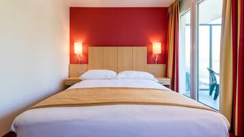 Une chambre d’hôtel avec un grand lit, deux lampes de chevet, une tête de lit en bois et une vue sur l’extérieur grâce à une grande fenêtre.