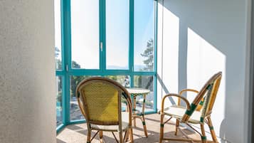 A balcony with wicker chairs and a small table, large windows, and a view of a pool and trees.