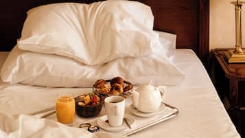 Ein ordentlich bezogenes Bett mit weißen Leinentüchern, ein Tablett mit Frühstücksgegenständen, darunter ein Teekessel, eine Tasse und eine Obstschale, sowie ein Nachttisch mit einer Lampe.