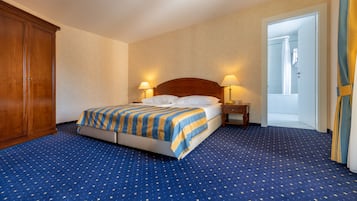 Camera d'albergo con un letto grande, due comodini, un armadio e un bagno visibile attraverso una porta aperta.