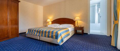 A hotel room with a large bed, two bedside tables, a wardrobe, and a bathroom visible through an open door.