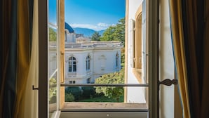 Vista desde una ventana con cortinas que muestra un edificio de arquitectura clásica y un balcón.