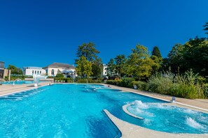 A large outdoor swimming pool with clear blue water, surrounded by greenery and a building in the background. - Grand Hôtel et Centre Thermal (Yverdon-les-Bains)
