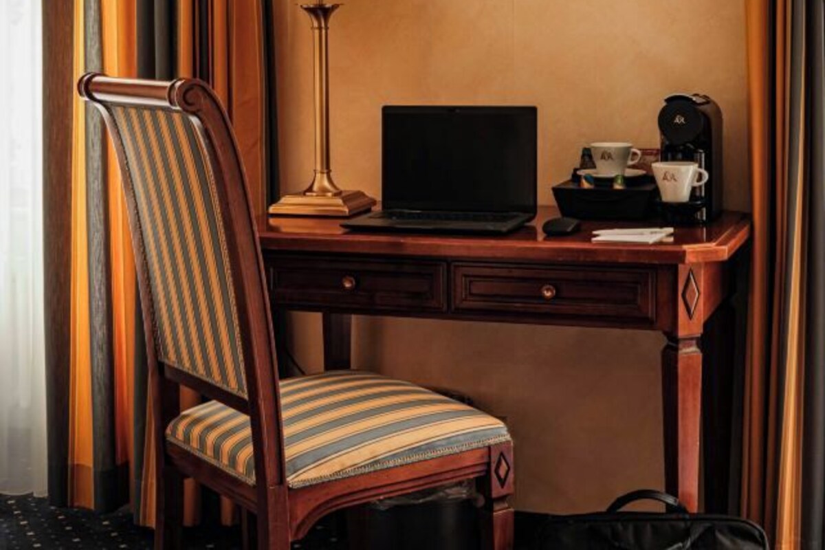 A wooden desk with a laptop, a coffee maker, and a cup.