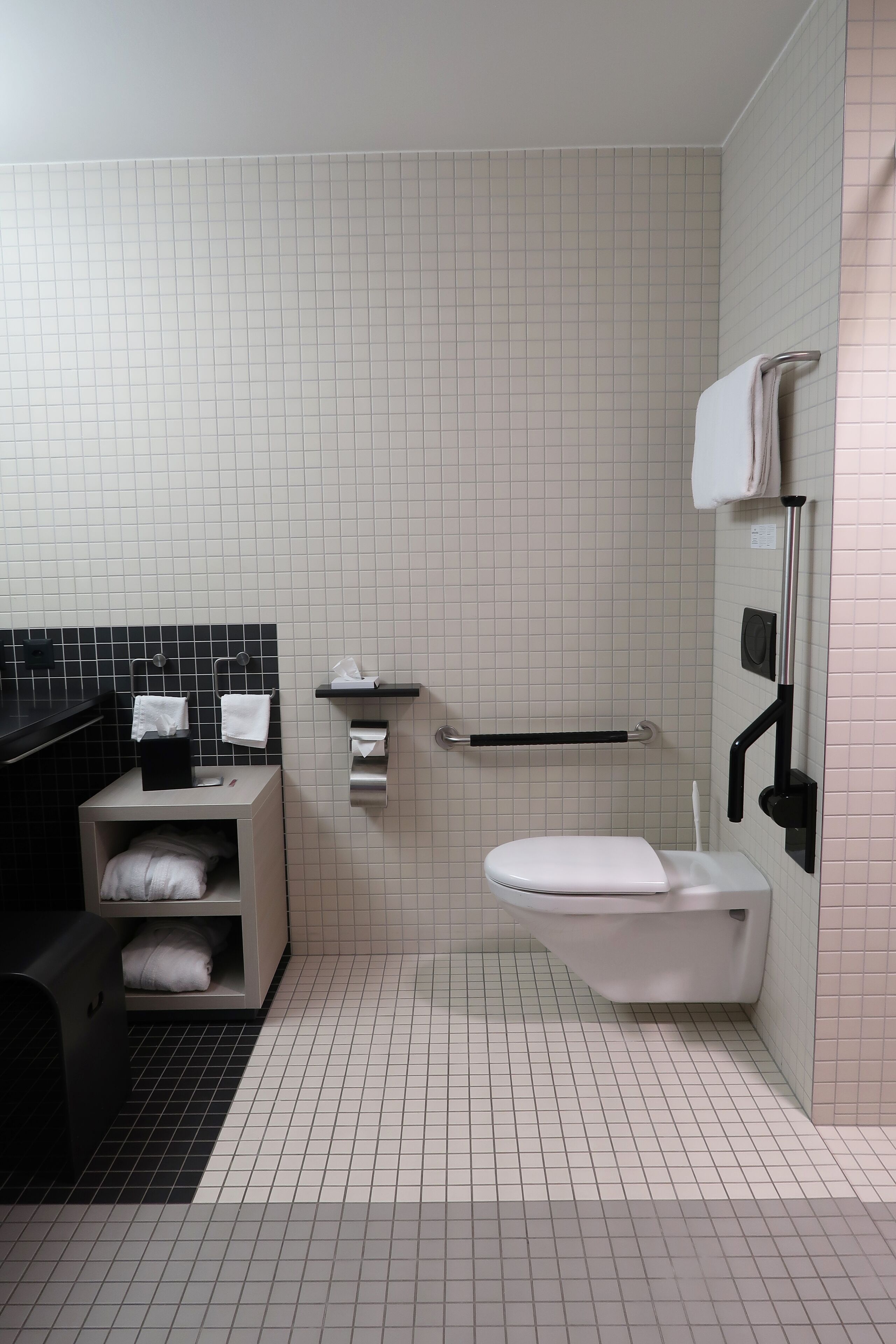 A modern bathroom with a white toilet, a black bathtub, a towel rack, and a hand dryer.