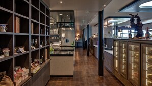 A modern hotel corridor with wooden flooring, glass display cases, and a central island with a bar area.