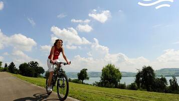 A person riding a bicycle on a paved path with a scenic view of a lake and hills in the background.