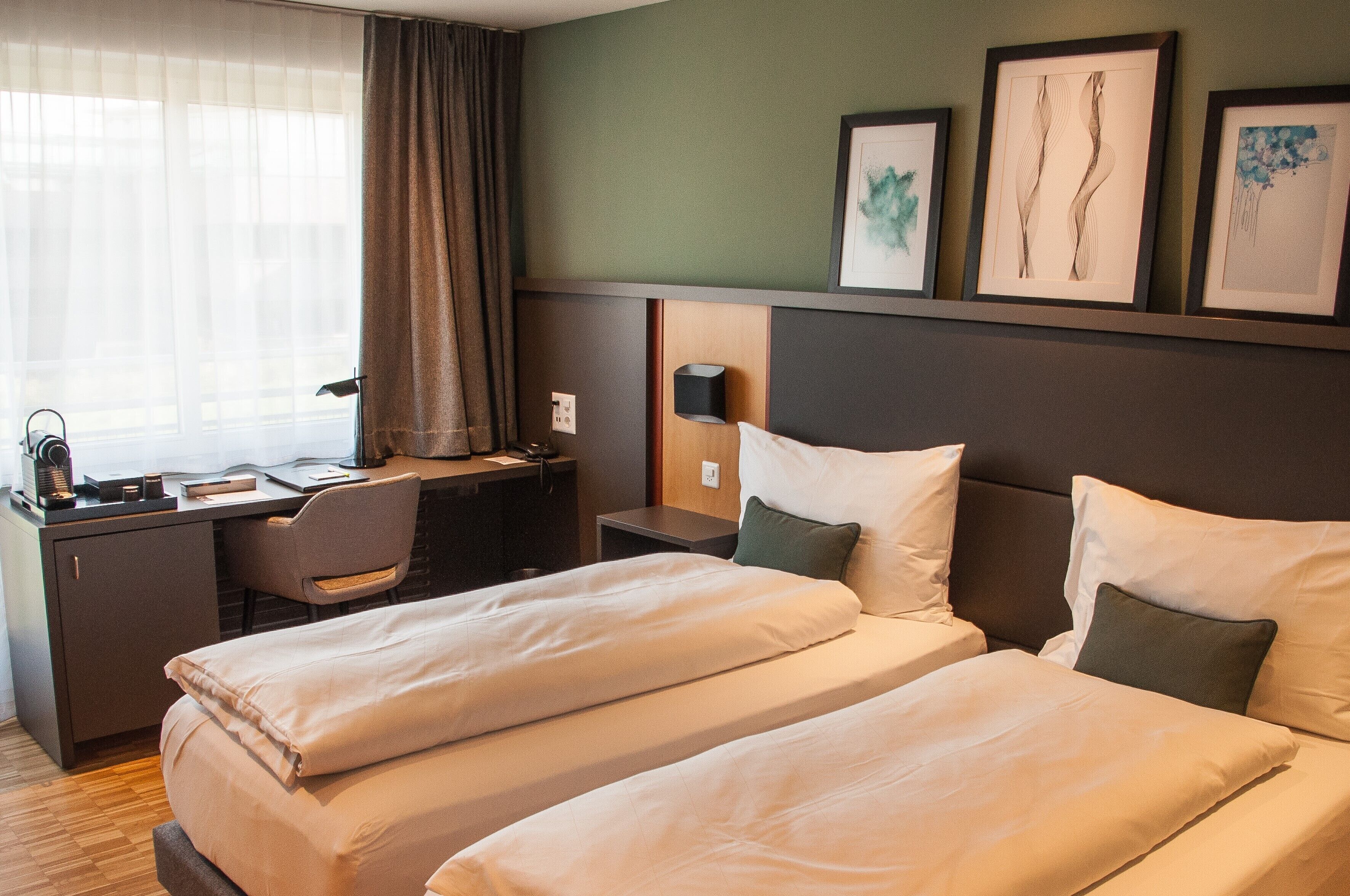 A hotel room with two beds, a desk, a chair, and a nightstand.