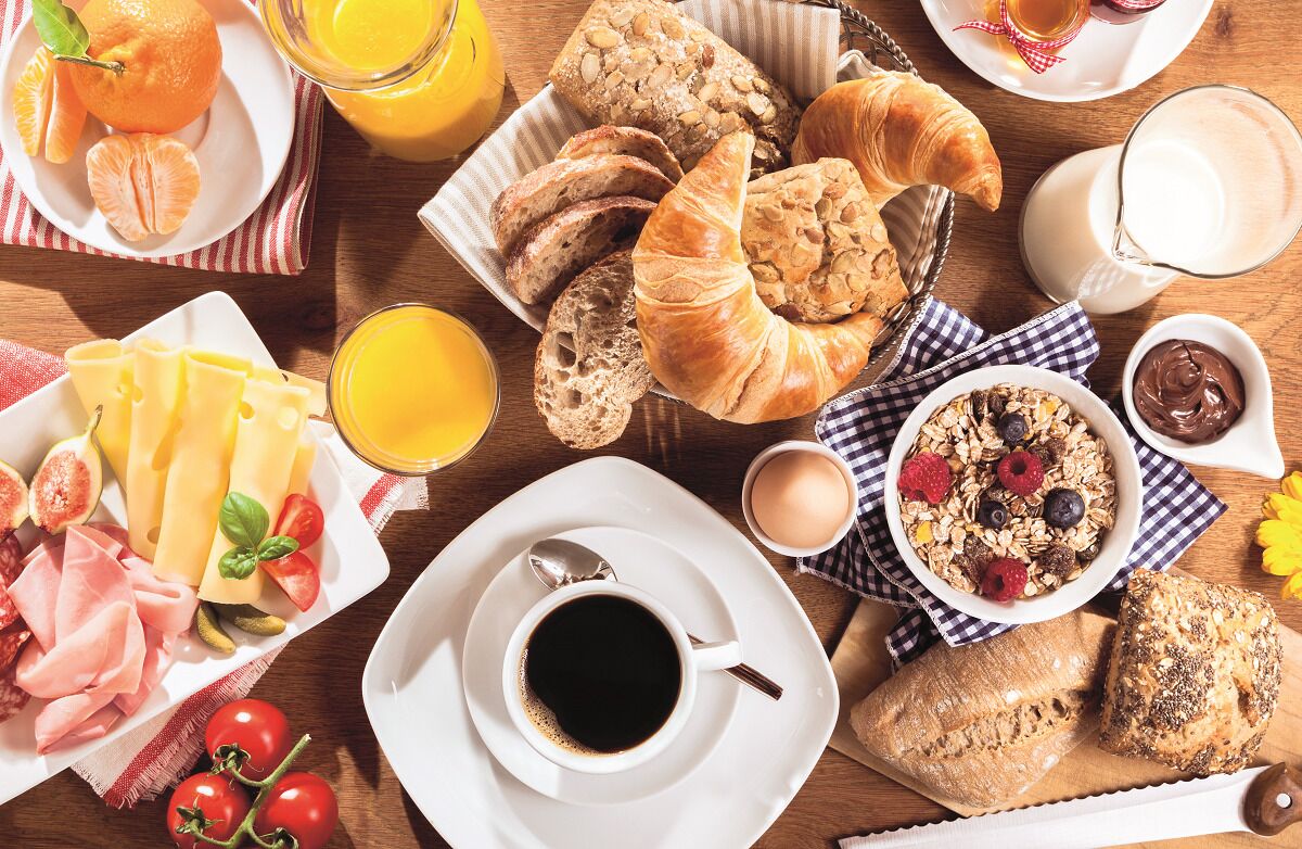 A breakfast table with croissants, orange juice, coffee, cheese, and various fruits.