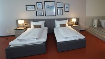 A hotel room with two beds, a headboard, bedside tables with lamps, a wall-mounted phone, and framed artwork.