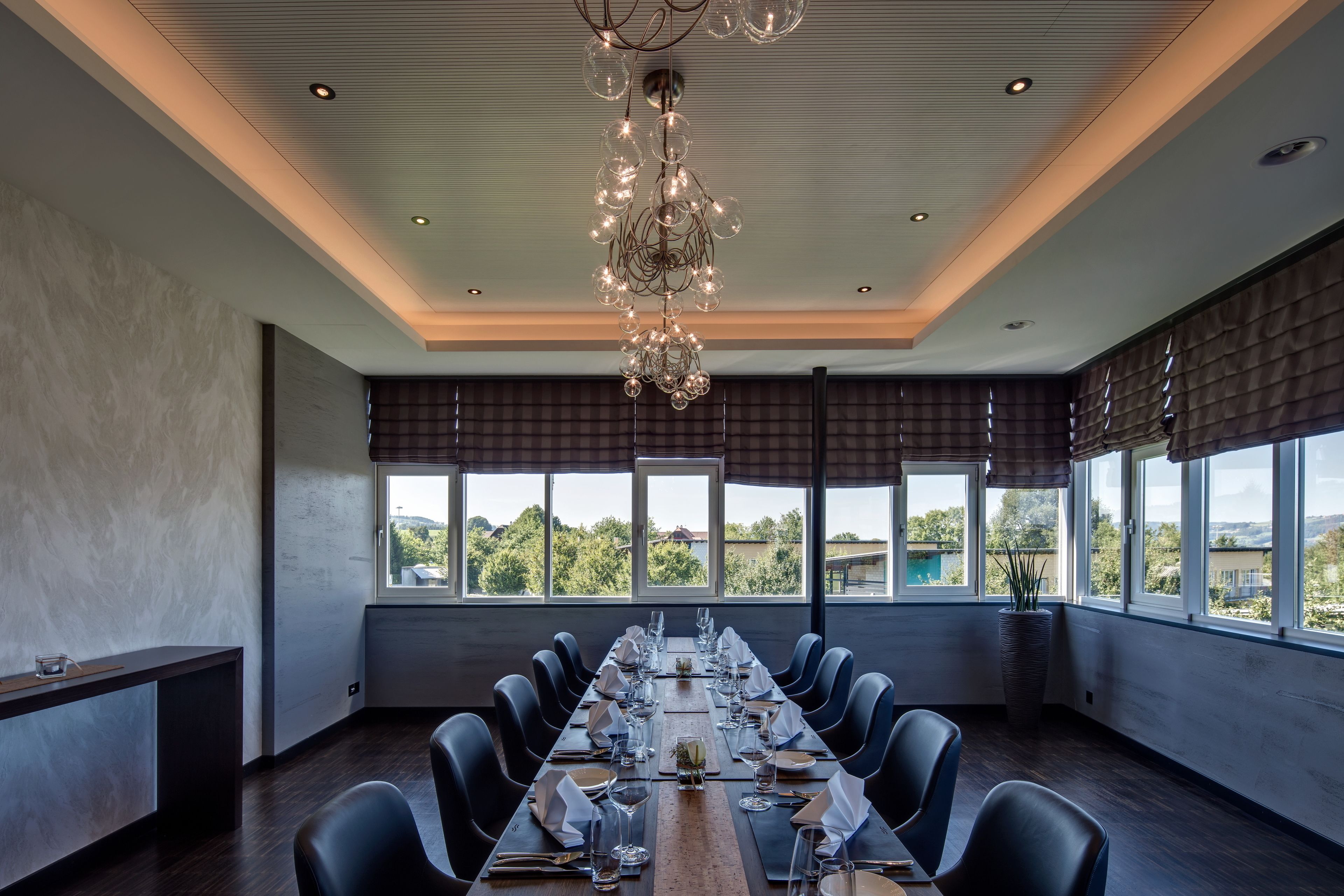 A conference room with a long table set for a meeting, large windows with a view, and a modern chandelier.
