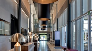 A modern hotel lobby with a long reception desk, large black pendant lights, and a wooden floor.
