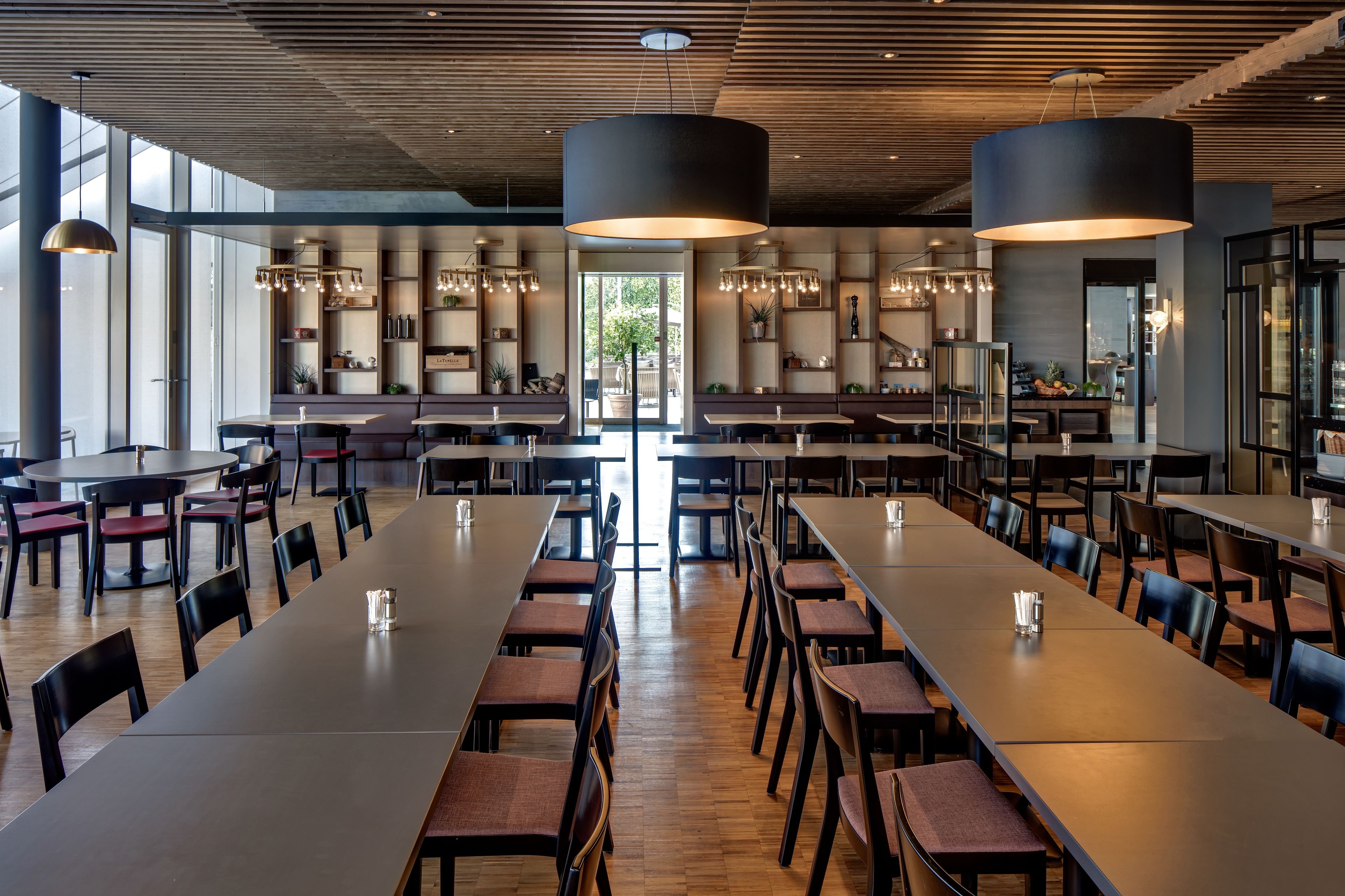 Un comedor amplio con mesas y sillas largas, iluminación colgante moderna y vistas al exterior.