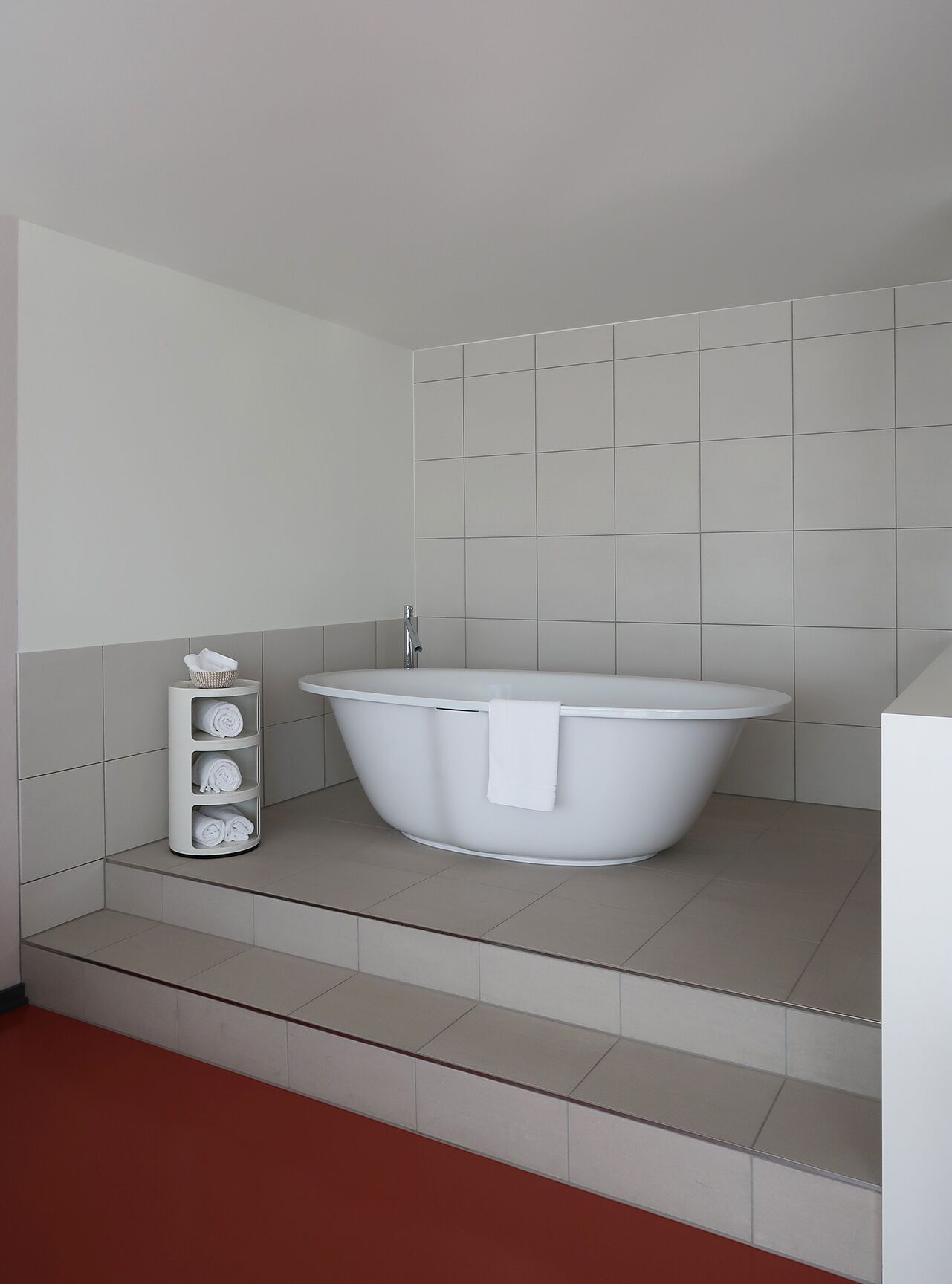 A modern bathroom with a freestanding bathtub, a towel rack with folded towels, and a small basket.