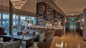 A modern bar area with a long counter, bar stools, and a variety of bottles and glasses.