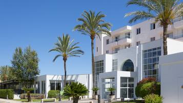 Un bâtiment moderne à étages, doté de grandes fenêtres et d’une pelouse bien entretenue agrémentée de palmiers.