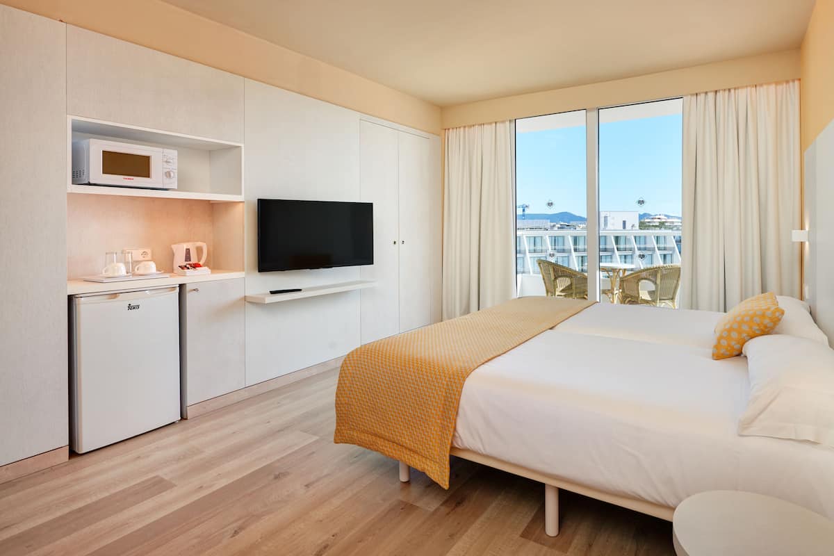 Ein Hotelzimmer mit Bett, Fernseher, Minibar und Blick auf die Stadt.