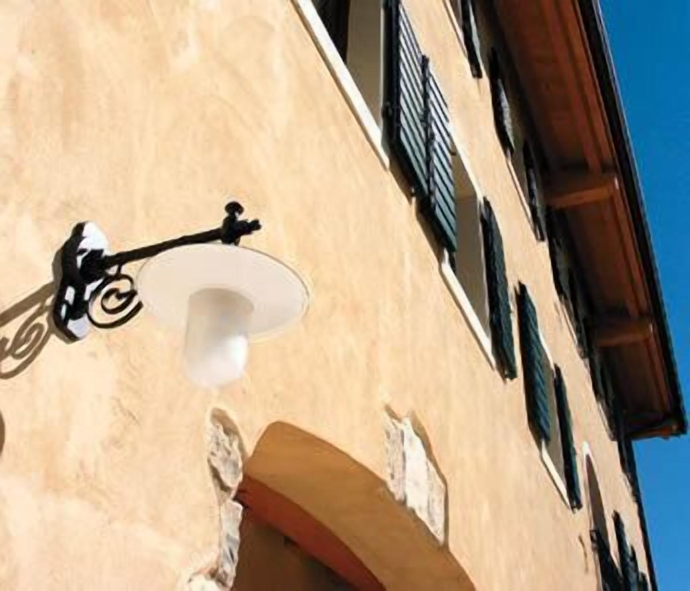 Un edificio con un lampadario a parete, una finestra con persiane e una vista parziale di un balcone.