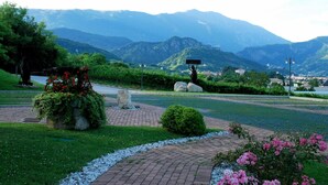 Un jardín ajardinado con una estatua, un camino empedrado y vistas a montañas distantes.