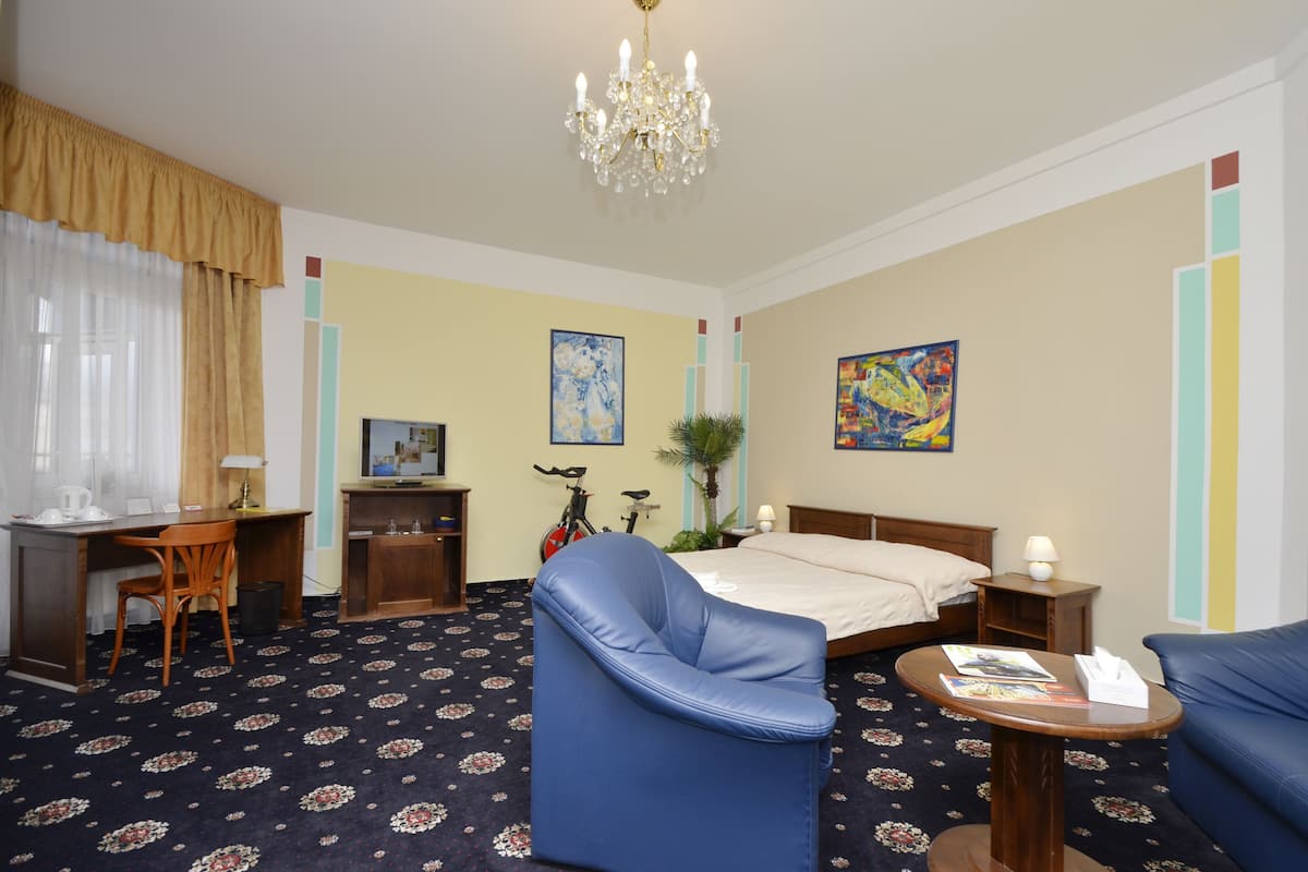 Une chambre d’hôtel comprenant un lit, un bureau, une chaise, une petite table, un lustre et des œuvres d’art accrochées aux murs.