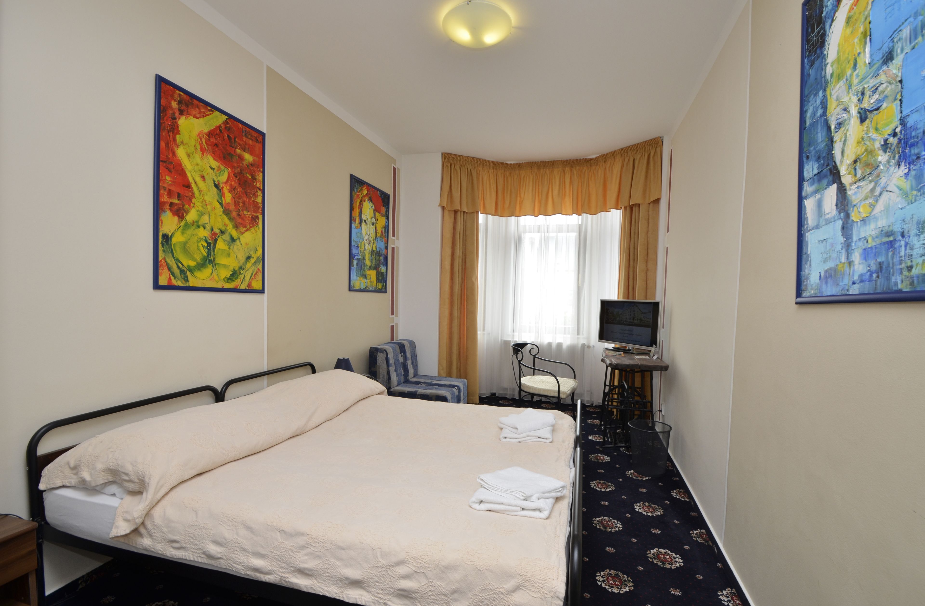 Ein Hotelzimmer mit einem Bett, einem Schreibtisch mit Computer, einem Stuhl und Bildern an der Wand.
