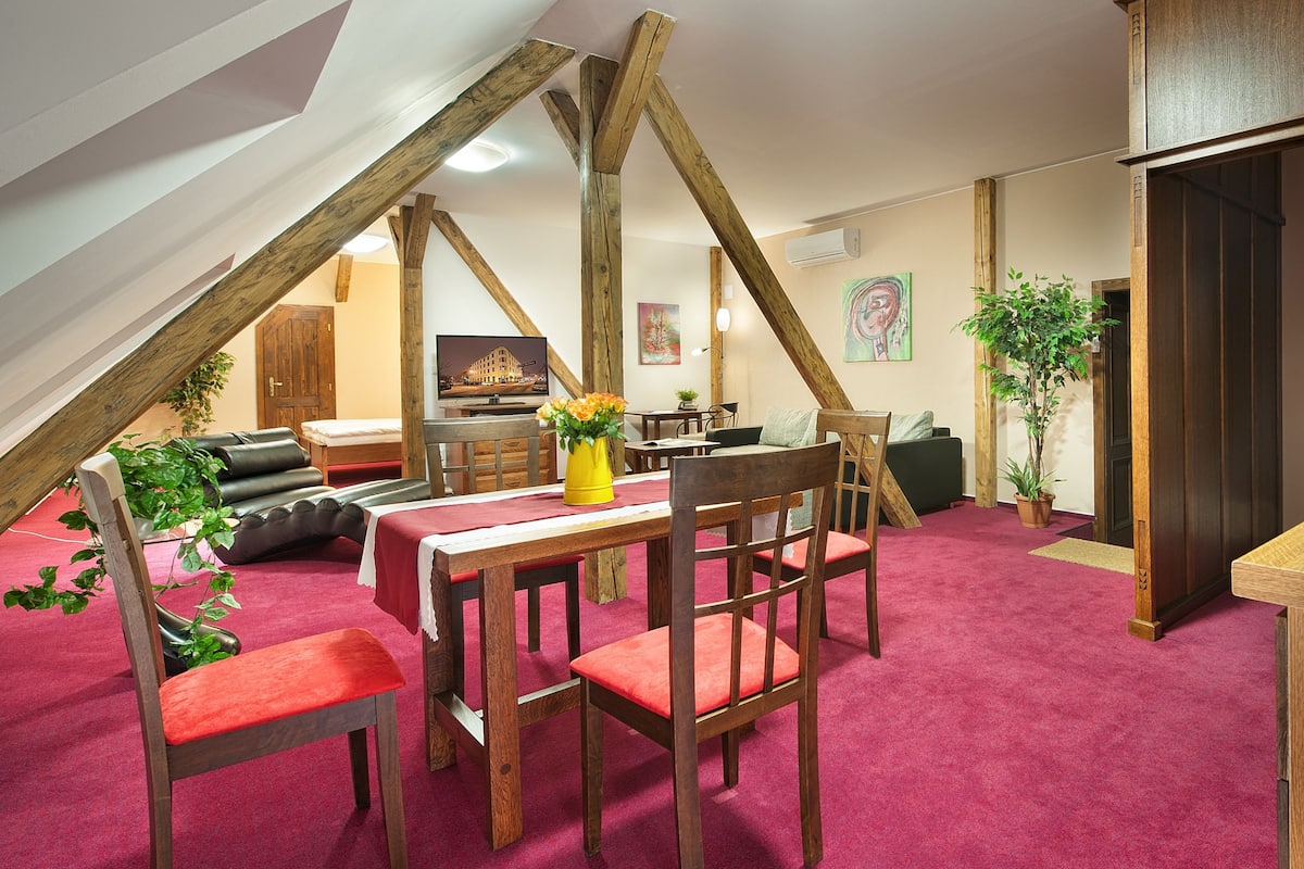 Une pièce confortable de style loft, comprenant un coin repas, des poutres apparentes, une cuisine avec une cuisinière intégrée et une moquette rouge.