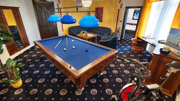 A pool table with balls, a sofa, a desk with a laptop, a bicycle, and a plant.