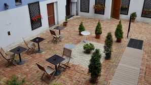 Un patio con suelo de ladrillo, mobiliario exterior, plantas en macetas y una pequeña fuente.